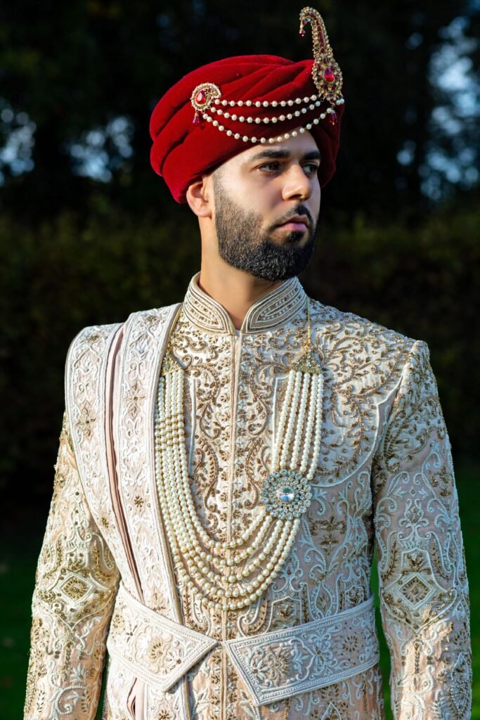 Groom in an ivory hand-embroidered sherwani with a red turban and pearl malas, dressed for the main wedding day