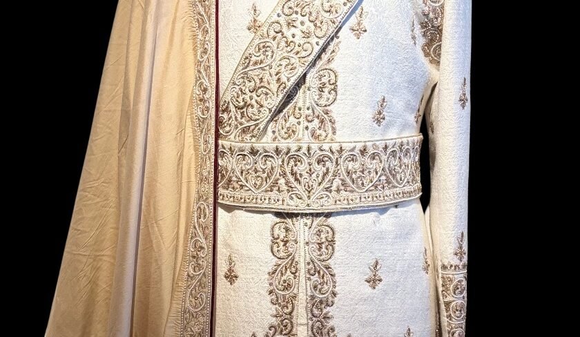 A matched embroidered belt fastened at the waist of an ivory worked sherwani